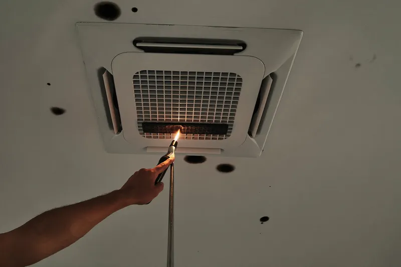 Technician checking an AC return grille with a torch and inspection camera beside dark ceiling spots